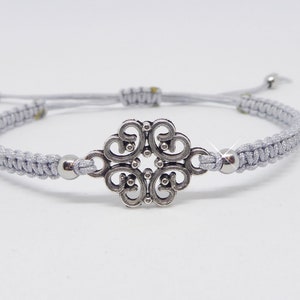 Peut inclure: Un bracelet tressé gris avec un charme argenté en forme de trèfle à quatre feuilles.