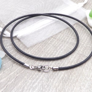 Könnte beinhalten: Eine schwarze Lederkordelkette mit einem silbernen Verschluss. Die Kette liegt auf einer Holzoberfläche.