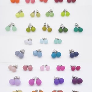 May include: A collection of colorful stud earrings in various shades, including white, yellow, orange, pink, red, green, blue, purple, and brown. Each pair features a small, round, matte-finish bead with a silver-colored post.