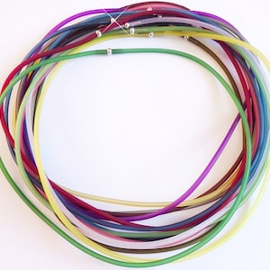 Könnte beinhalten: Eine Sammlung bunter, durchsichtiger Gummikordeln, die in einem Kreis angeordnet sind, mit dazwischen verteilten silbernen Perlen.