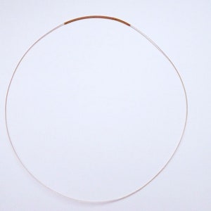 May include: A delicate necklace featuring a thin, silver-colored chain with a small, copper-colored accent. The necklace is circular in shape, resting against a white background. The minimalist design suggests a focus on simplicity and elegance.