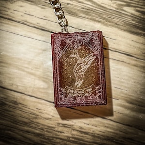 May include: A red and gold keychain with a silver chain and a small, detailed image of a bird with the text "The Future is Now" on it.