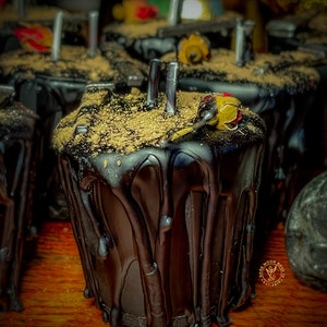 May include: Black wax candle with a gold glitter top and a small red flower on top. The candle is dripping wax and has a dark moon rose logo on the side.