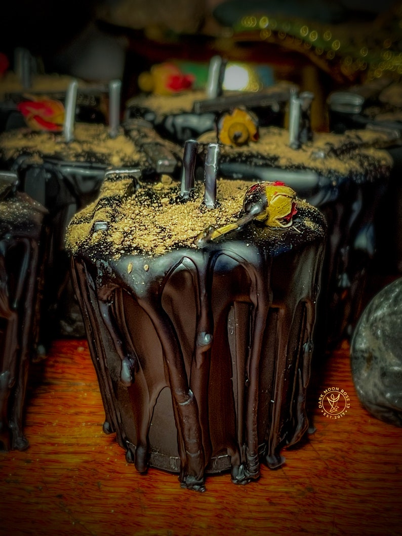 May include: Black wax candle with a gold glitter top and a small red flower on top. The candle is dripping wax and has a dark moon rose logo on the side.