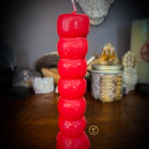 May include: A red, multi-sectioned candle with a pointed top. The candle is on a wooden surface.