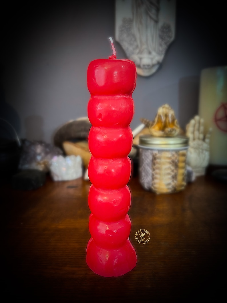May include: A red, multi-sectioned candle with a pointed top. The candle is on a wooden surface.