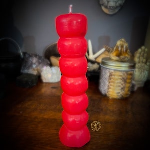 Puede incluir: Una vela roja de varios niveles con una mecha blanca. La vela tiene forma de esferas apiladas.