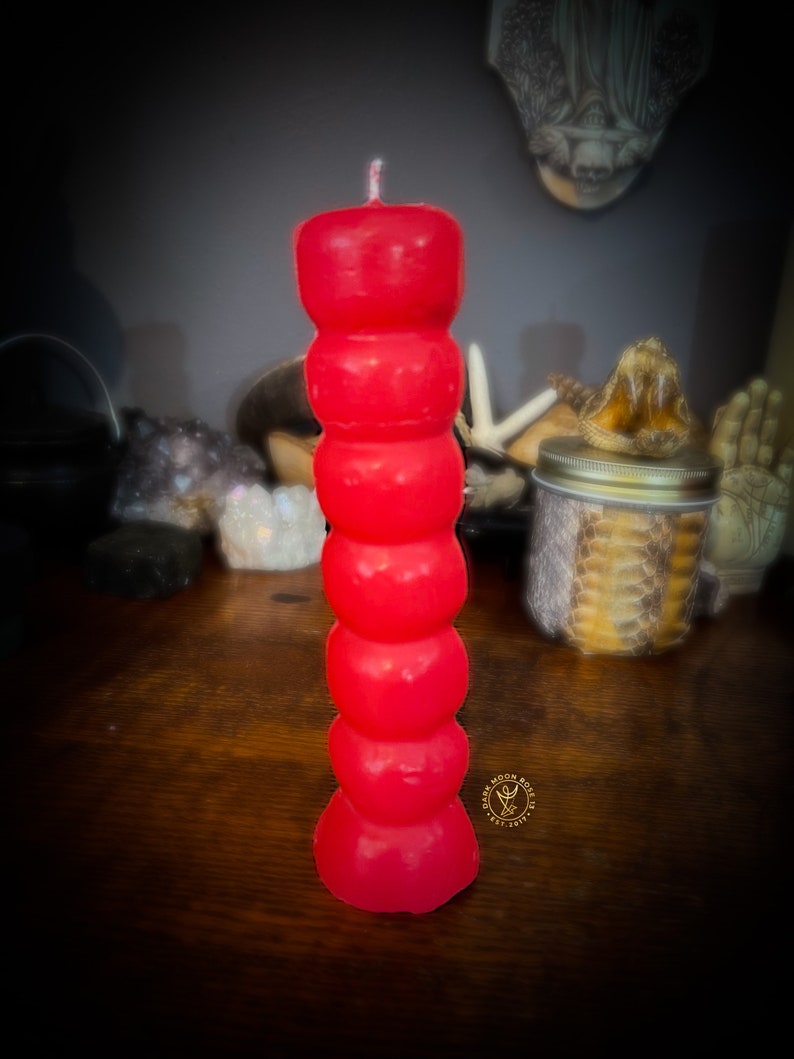 May include: A red, multi-layered candle with a white wick. The candle is shaped like a series of stacked spheres.