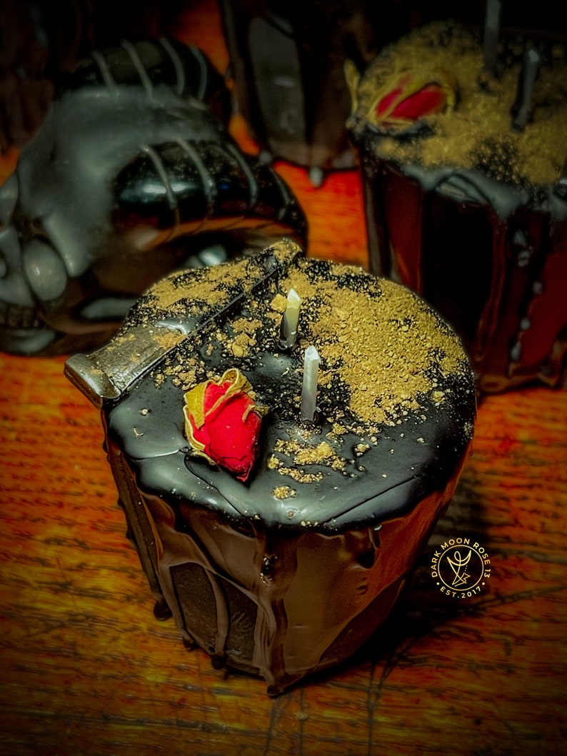 May include: Black candle with a red rose and gold flakes on top. The candle is dripping wax and has a label that says "Dark Moon Rose Est. 2017".