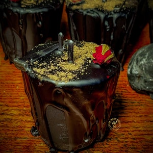 May include: Black candle with a red rose on top, covered in a thick layer of dark chocolate. The candle is sitting on a wooden surface.