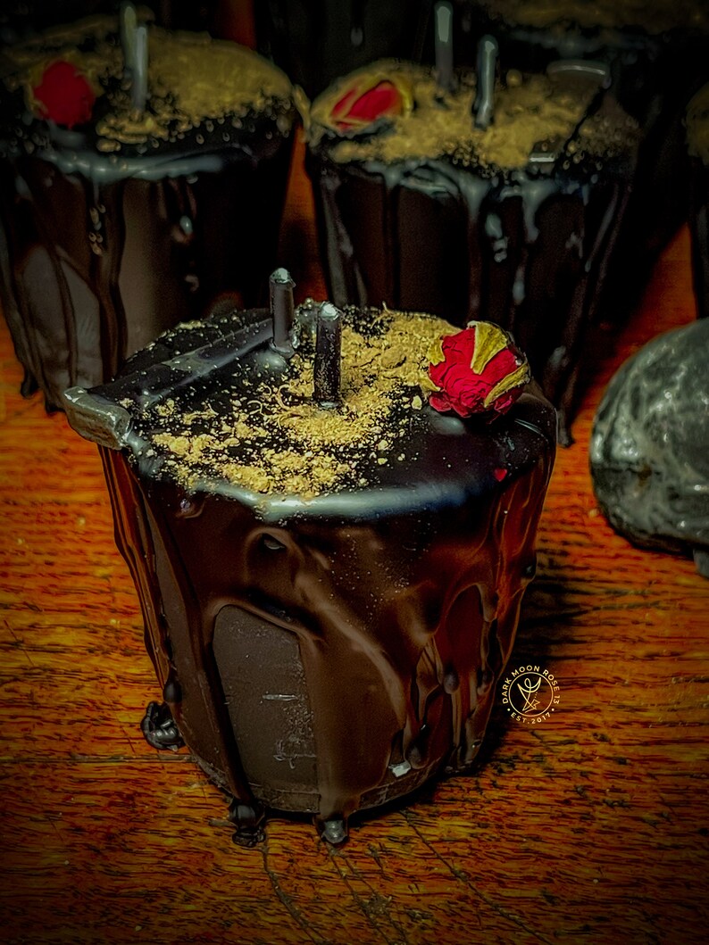 May include: Black candle with a red rose on top, covered in a thick layer of dark chocolate. The candle is sitting on a wooden surface.