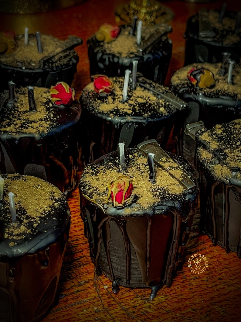 May include: A group of black candles with gold glitter and dried rose petals on top. The candles are arranged in a circle on a wooden surface.