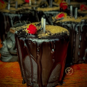 May include: A black candle with a red rose on top and gold glitter. The candle is dripping wax and has a label that says "Dark Moon Rose Est. 2017".
