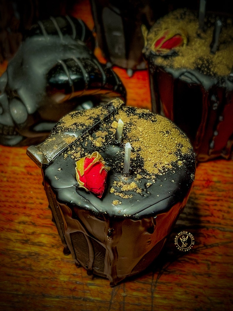 May include: Black candle with gold flakes and a red rose on top. The candle is dripping wax and has a gold label that says "Dark Moon Rose 13 Est. 2017".