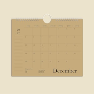 May include: A tan wall calendar for December 2027 with a spiral binding and a circular hanging hole. The grid displays days from Sunday to Saturday, numbered 1 through 31. The text includes the year 2027, the month December, and listed holidays.