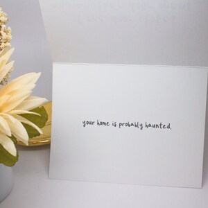 May include: A white card with the text "your home is probably haunted." written in black ink.