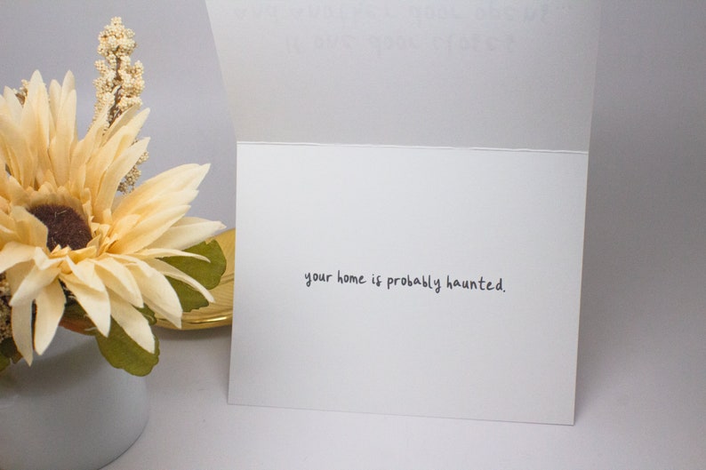 May include: A white card with the text "your home is probably haunted." written in black ink.