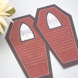 May include: Two red coffin-shaped note cards with black borders and a white moth graphic in the top center. The cards have lined writing space.