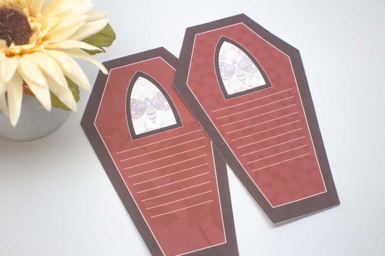 May include: Two red coffin-shaped note cards with black borders and a white moth graphic in the top center. The cards have lined writing space.