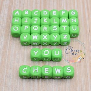 May include: Green alphabet letter beads with white letters spelling out "YOU CHEWS" on a wooden background.