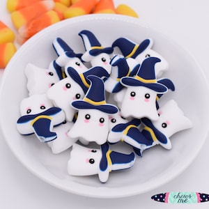 May include: A bowl filled with white and blue silicone Halloween ghost charms. The ghosts have black eyes and a small smile. Each ghost is wearing a blue witch hat with a yellow brim.