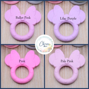 K&ouml;nnte beinhalten: Vier Silikon-Bei&szlig;ringe in Form eines Minnie Mouse-Kopfes mit Schleife. Die Bei&szlig;ringe sind in den Farben Balletrosa, Lila, Rosa und Hellrosa.