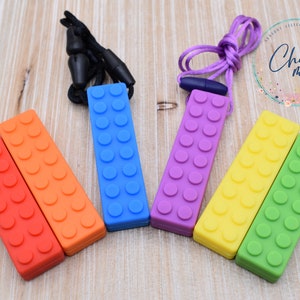 May include: Colorful, brick-shaped sensory chew toys in red, orange, blue, purple, yellow, and green. Each chew toy has a textured surface with rounded bumps, and some are attached to a lanyard. The logo "Chews Me" is visible.
