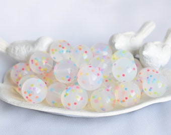 May include: A collection of translucent white silicone beads with colorful confetti embedded inside. The beads are arranged in a white ceramic dish.