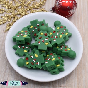 May include: A white plate filled with green silicone Christmas tree beads. The beads are decorated with red, white, and yellow details.