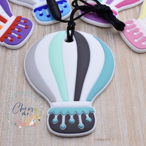 May include: A white, gray, black, and teal silicone hot air balloon teether with a black cord. The balloon has a gray and teal striped pattern and a black and teal bottom with a row of teal hearts.