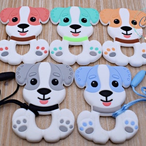May include: Five silicone puppy teething toys in different colors, including orange, green, blue, and gray. Each toy has a white body with a black nose and eyes. Two of the toys have a black cord attached to them.