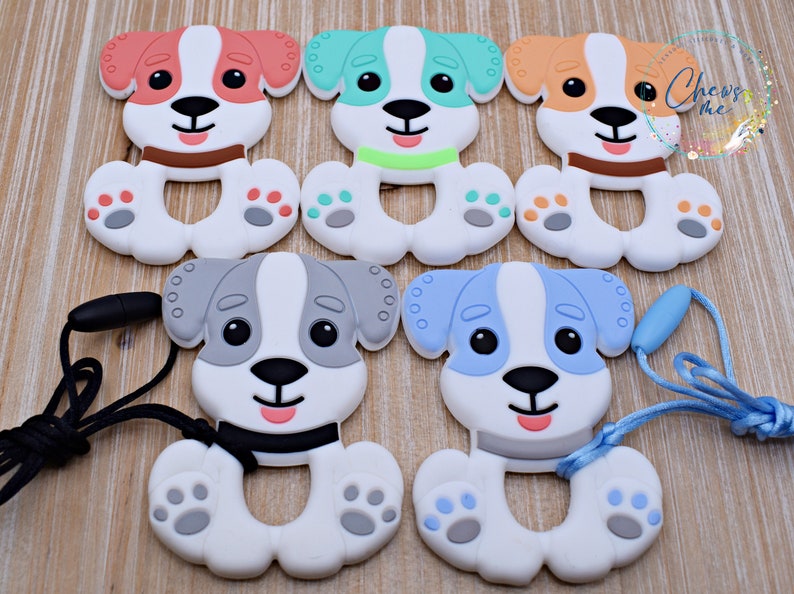 May include: Five silicone puppy teething toys in different colors, including orange, green, blue, and gray. Each toy has a white body with a black nose and eyes. Two of the toys have a black cord attached to them.