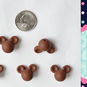 May include: Five brown silicone teether beads shaped like Mickey Mouse heads. The beads are about the size of a US quarter.