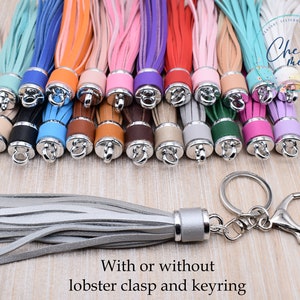 May include: A variety of colorful leather tassels with silver metal caps and lobster clasps. Some tassels have keyrings attached. The text "Chews Me" is visible in the background. The caption "With or without lobster clasp and keyring" is below the tassels.