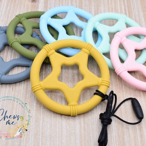 May include: A set of six silicone teethers in various colors, including gray, green, blue, yellow, and pink. Each teether is shaped like a star with a hole in the center and has a textured surface. One teether has a black cord attached to it.