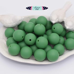 May include: A close-up of a pile of 25 green silicone beads. The beads are round and have a hole in the center. The beads are in a white dish with two white bird figurines on the edge.