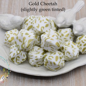 Peut inclure: Gros plan sur un ensemble de perles de dentition en silicone blanc avec un imprimé guépard doré. Les perles sont dans un plat blanc en forme de feuille. Le texte "Gold Cheetah (slightly green tinted)" est au-dessus des perles.