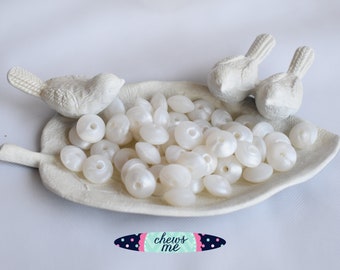 May include: A white ceramic leaf-shaped dish with two white ceramic bird figurines on the edge. The dish is filled with white pearl-like beads.