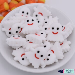 May include: A white bowl filled with white ghost-shaped silicone beads with black eyes and red smiling mouths. The beads are for sensory play and chewing.