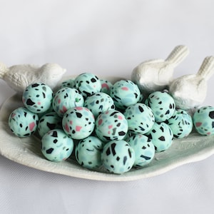 May include: A collection of teal blue and white speckled round beads in a white ceramic dish with two white bird figurines.
