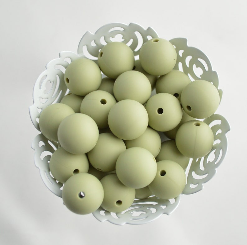 May include: A bowl filled with sage green silicone beads. The beads are smooth and round, and they are perfect for making jewellery or other crafts.
