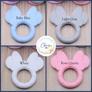 K&ouml;nnte beinhalten: Vier Silikon-Bei&szlig;ringe in Form einer Schleife mit einem Ring in der Mitte. Die Bei&szlig;ringe sind in den Farben Babyblau, Hellgrau, Wei&szlig; und Ros&eacute;gold.