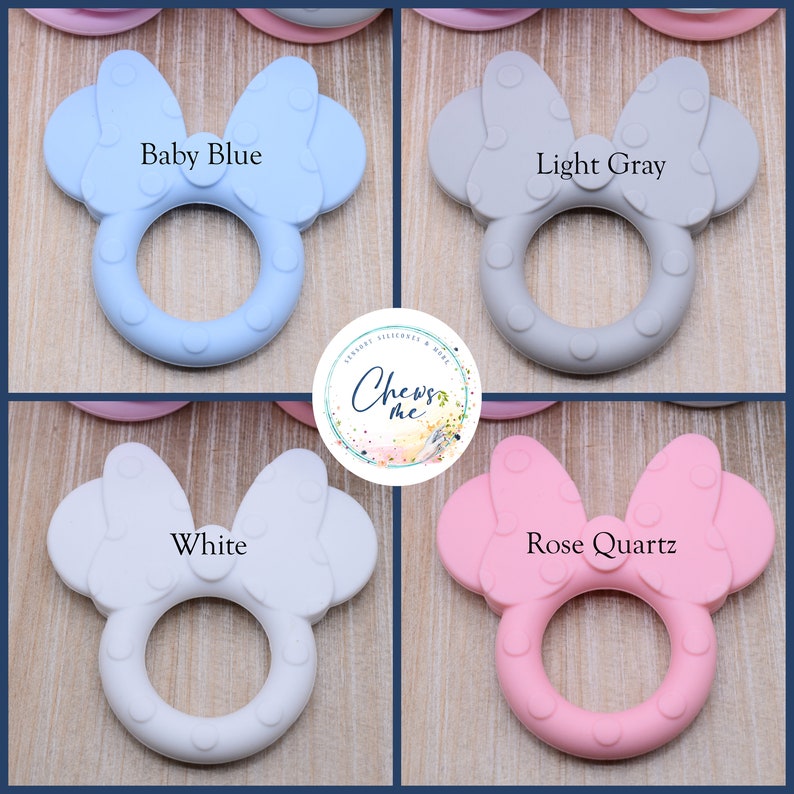 K&ouml;nnte beinhalten: Vier Silikon-Bei&szlig;ringe in Form einer Schleife mit einem Ring in der Mitte. Die Bei&szlig;ringe sind in den Farben Babyblau, Hellgrau, Wei&szlig; und Ros&eacute;gold.