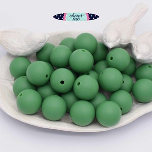 May include: A close-up of a pile of 25 green silicone beads. The beads are round and have a hole in the center. The beads are in a white dish with two white bird figurines on the edge.