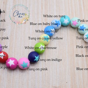 Puede incluir: Primer plano de un collar hecho de cuentas de silicona de colores con dise&ntilde;os en forma de estrella. Las cuentas son de varios colores, incluyendo rosa, azul, verde, amarillo y blanco. Cada cuenta tiene una combinaci&oacute;n de colores diferente, como blanco sobre rosa, azul sobre blanco y rosa sobre menta.