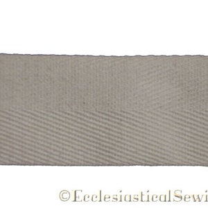 May include: A close-up of a white cotton twill tape with a herringbone weave. The tape is approximately 1 inch wide.