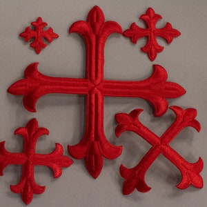 Könnte beinhalten: Ein Set aus sieben roten gestickten Kreuzen mit verzierten Designs. Die Kreuze sind in verschiedenen Größen und in einer Gruppe auf einem grauen Hintergrund angeordnet.