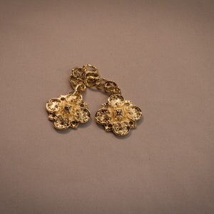 Puede incluir: Un par de cierres decorativos de metal dorado con diseños intrincados. Los cierres están conectados por una cadena.