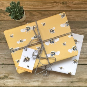 May include: Two gift boxes wrapped in yellow and white paper with a bee pattern. The boxes are tied with twine and have a gift tag attached.