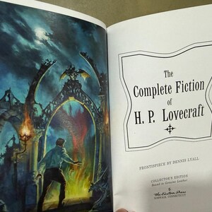 Puede incluir: Un libro abierto con una ilustraci&oacute;n en color y texto. La p&aacute;gina izquierda muestra a un hombre frente a un portal de fuego. La p&aacute;gina derecha muestra el t&iacute;tulo "The Complete Fiction of H.P. Lovecraft" en un marco decorativo. Es una edici&oacute;n de coleccionista.
